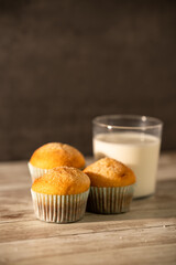 Glass of milk with three freshly baked muffins in the foreground - breakfast, snack, pastries concept