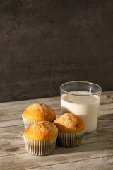 Glass of milk with three freshly baked muffins in the foreground - breakfast, snack, pastries concept