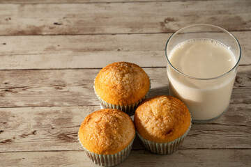 Glass of milk with three freshly baked muffins in the foreground - breakfast, snack, pastries concept