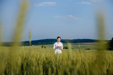 Fototapeta premium Scientist technologist in a white coat on a young wheat field writes down data on this year's crop on a smart tablet