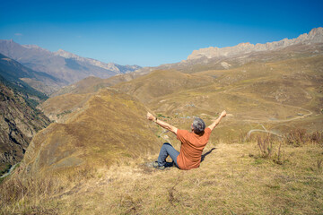 A man in the mountains with open arms looks into the distance, enjoying the scenery of the mountains.