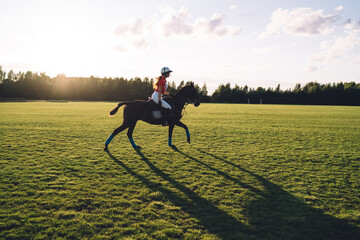 Young horsewoman in polo uniform trotting on playing field