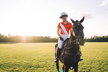 Young horsewoman in polo uniform riding mare on playing field