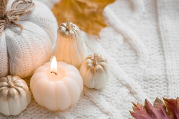 Still-life. Knitted pumpkin, autumn leaves, white knitted plaid and a burning candle in the shape of a pumpkin. Cozy autumn concept.
