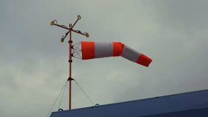 Windsock. Wind designator on a metal pole with red and white lights. A pole with a wind indicator on blue roof.