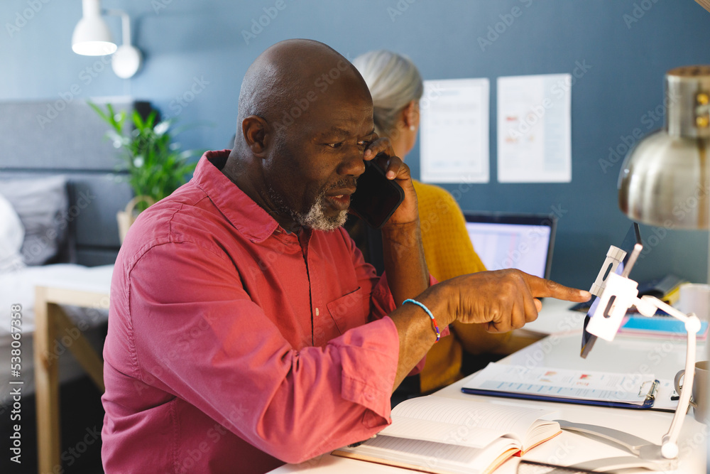 Wall mural Senior diverse couple sitting at table and working