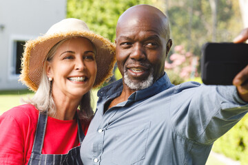 Happy senior diverse couple taking selfie in garden