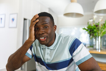 Happy african american man making video call smiling to camera holding head in kitchen