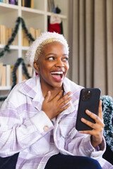 Happy african american woman wearing santa claus hat, using smartphone for video call