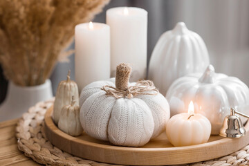 Fototapeta na wymiar Still-life. Knitted pumpkin, pampas grass, pumpkin-shaped candles and white ceramic pumpkins on a wooden tray on a coffee table in the home interior of the living room. Cozy autumn concept.