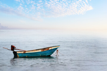 Naklejka na ściany i meble A small fishing boat floating in the ocean with summer morning bright sky and clouds image for background use.