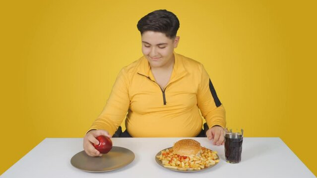 Obese boy choosing between hamburger and apple. Healthy food choice.
The obese child who wants to eat a hamburger prefers an apple.
