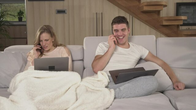 CLOSE UP: Married couple annoying each other at remote work during pandemic time. Young partners being busy using laptops and smartphones while working at home. Twosome working at home in isolation.