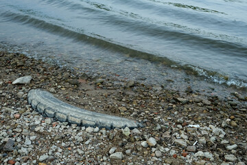 Pollution of rivers and water areas. Environmental problems, recycling of car tires. Used tire was discarded on the riverbank