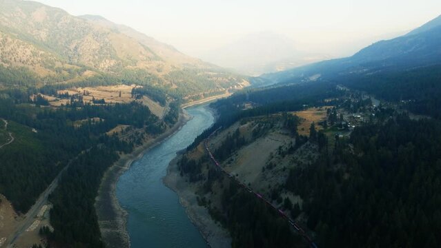 A train moving along the Fraser River in British Columbia. The interior of BC near Lytton and Kamloops, as a train moves through the valley. Sunrise aerial shot of the Fraser River.