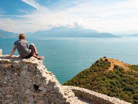 Tired blond hair boy it on the stony wall of ruin Rocca di Manerba