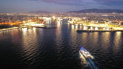 Aerial drone night shot of passenger ferry arriving to famous passenger port of Piraeus one of the largest in Europe, Attica, Greece