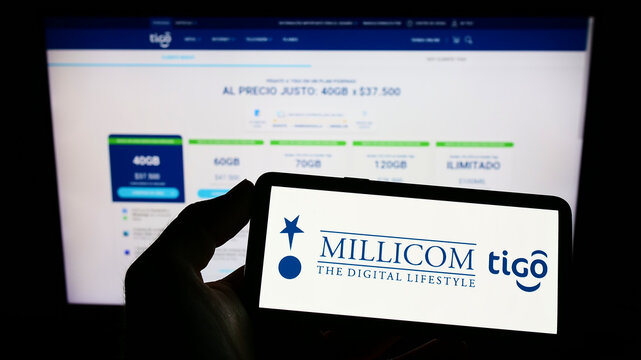Stuttgart, Germany - 10-03-2022: Person holding mobile phone with logo of company Millicom International Cellular SA on screen in front of web page. Focus on phone display.