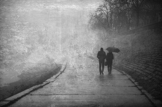 Couple walking beside river in rain and mist on a cold autumn day
