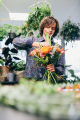 Young man arranges bouquet from flowers in florist shop. - obrazy, fototapety, plakaty