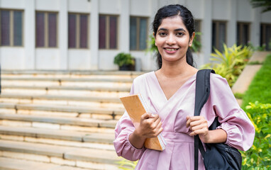 Closeup of shot Happy young girl with backpack holding book by smilling at camera at college campus...