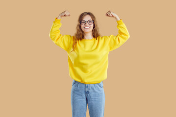 Cheerful teenage girl shows her biceps in funny way as sign of her strength, success and health....