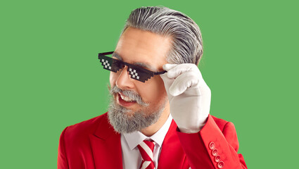 Man in funny costume. Head shot of confident adult man with gray hair and beard in thug life glasses, white gloves, stylish red suit and tie isolated on green background. Christmas fashion concept