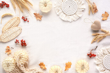 Off white textile background with frame from natural Fall decorations. Flat lay, top view. Pumpkins in net bag, dry leaves, macrame pads, wattle leaves, wheat ears. Copy-space, place for text.