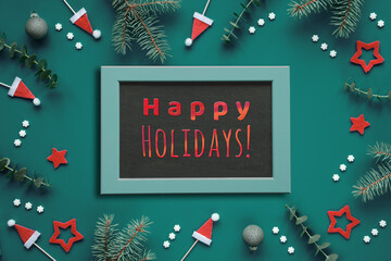 Greeting text Happy Holidays on blackboard, chalk board. Dark teal green background with fir and...