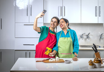 Mother and daughter duo in a kitchen, taking a selfie while chopping a paneer