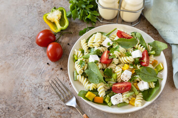 Italian food - Salad with gluten free pasta, spinach, tomatoes, beans and feta cheese on a stone table. Healthy food, vegetarian appetizer. Copy space.