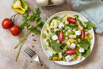 Italian food - Salad with gluten free pasta, spinach, tomatoes, beans and feta cheese on a stone table. Healthy food, vegetarian appetizer. View from above.