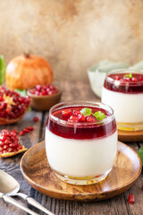Winter delicious italian dessert panna cotta with pomegranate jelly and mint, homemade cuisine on a wooden background. Copy space.