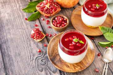 Winter delicious italian dessert panna cotta with pomegranate jelly and mint, homemade cuisine on a wooden background. Copy space.