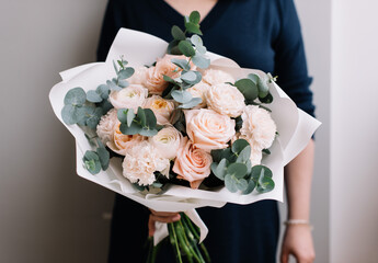 Very nice young woman holding big and beautiful bouquet of fresh roses, carnations, eucalyptus flowers in pastel pink colors, cropped photo, bouquet close up - 538087102
