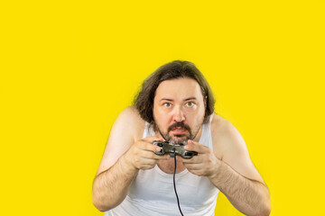 A disgruntled unshaven man in a white undershirt angrily plays a computer game with a gamepad. Unemployed slovenly dressed man from Eastern Europe.