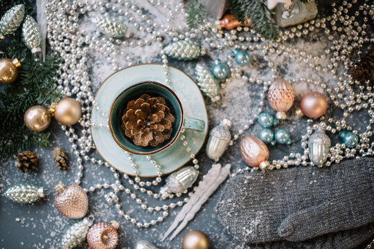 Beautiful festive winter set: pine cone in a cup, ornaments, beads, spruce branches, fake snow, glitter on the grey table background, close up view © anastasianess