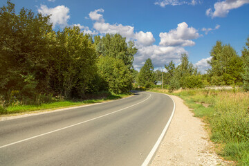 Close-up of a small empty highway in the countryside. Road turning between trees. Suburban asphalt two-lane road.