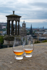 Two glasses of single malt scotch whisky and view from Calton hill to park and old parts of Edinburgh city in rainy day, Scotland, UK