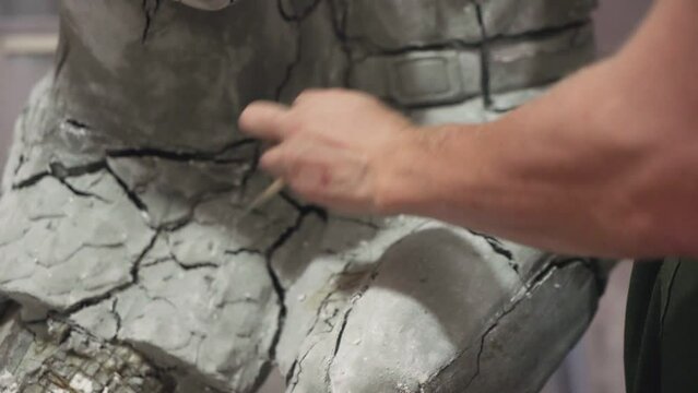 Close up of male sculptor uses brush to clean plaster structural of woman