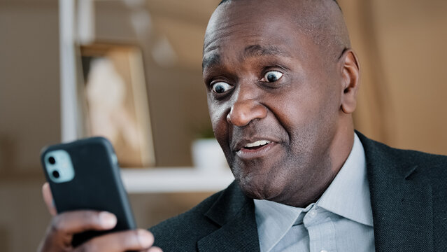 African American Old 50s Surprised Amazed Shocked Man Looking At Mobile Phone Screen Reading Unbelievable News Waving Head No Disagreement Negation Refusal Shock Fear Amazing Online Sms Shock Reaction