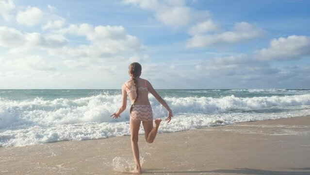 A Happy teenage girl with long hair runing along the coast of the Atlantic Ocean and jumping high. Full HD slow motion video of a child playing on the beach.