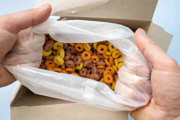 hands open a box of cereal corn rings 