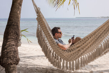 man using smartphone on the beach in hammock, internet connection