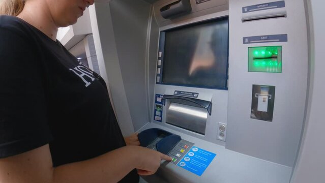 A woman withdraws money from an ATM. A girl using an automated teller machine. Close-up. A woman tourist withdraws cash from an ATM in the city