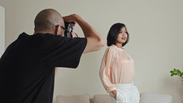 Professional photographer taking pictures of Asian fashion model in elegant pastel outfit as she posing in studio