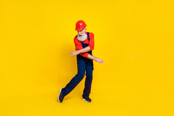 Fototapeta na wymiar Photo of good mood cool senior guy dressed uniform overall red hardhat having fun dancing isolated yellow color background