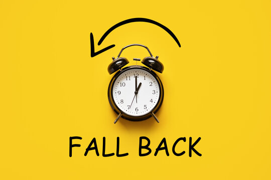 Daylight saving day. Fall Back. Black Alarm clock and autumn leaves and text Fall Back on yellow background. Daylight saving time end