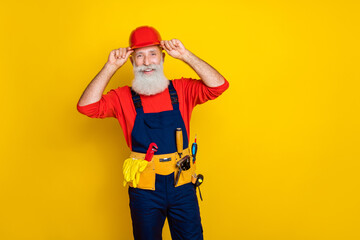 Photo portrait of handsome grandparent arms touch helmet toolbelt maintenance dressed safety uniform isolated on yellow color background