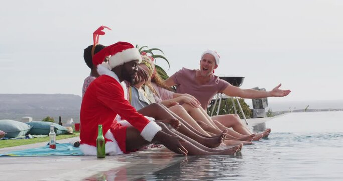 Six diverse happy friends celebrating christmas in costumes, outdoors with feet in swimming pool